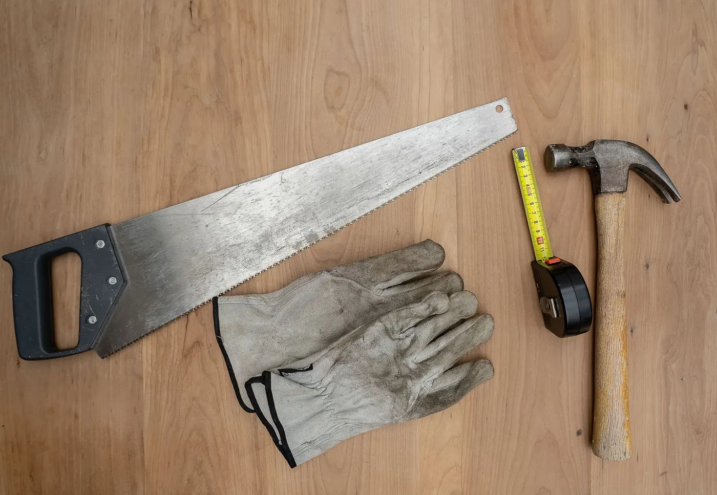 Hand saw, hammer, tape measure and work gloves on a wooden surface